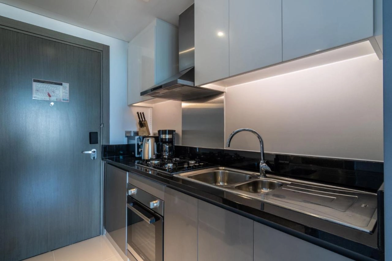 Modern studio apartment interior at Damac Maison Prive in Business Bay, Dubai, showing a well-equipped kitchenette, cozy sleeping area, and living space with large windows overlooking the city.